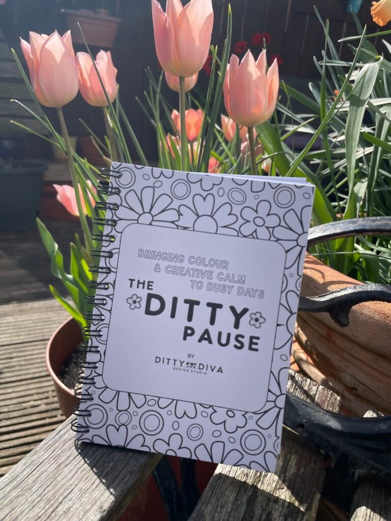 Photo of The Ditty Pause Colouring Book on a garden bench with pretty salmon coloured tulips behind it.